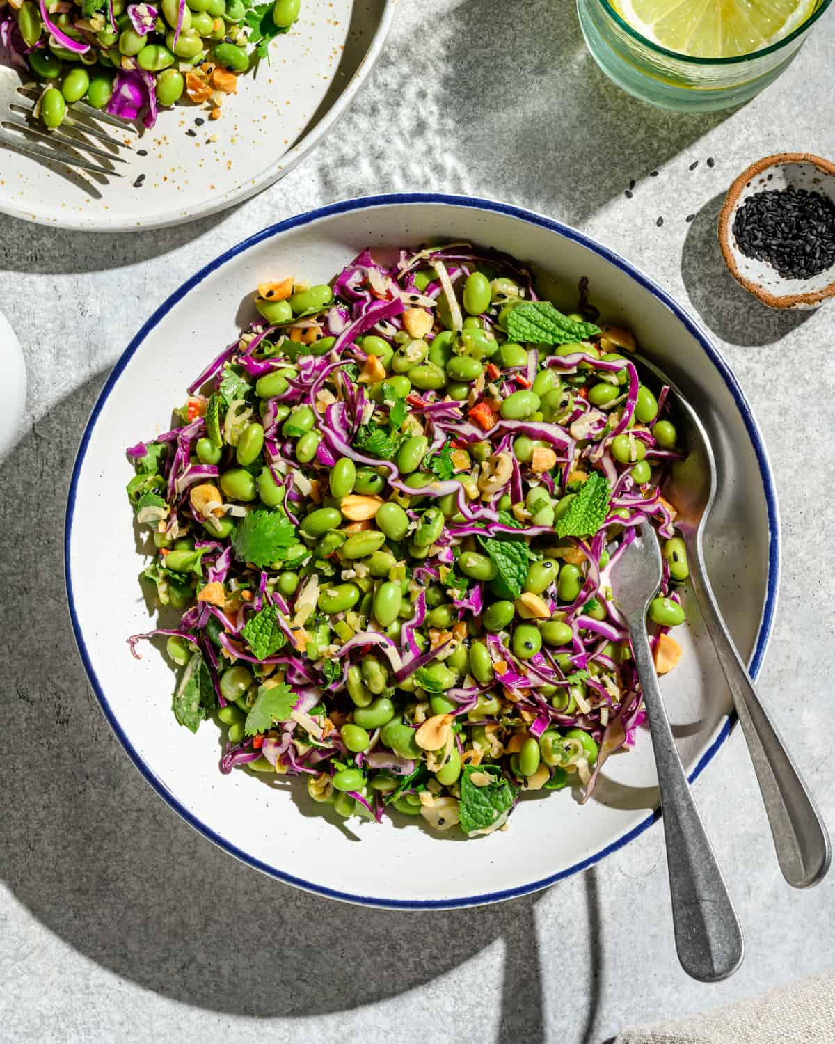 Bowl of edamame salad with two spoons on a white table.