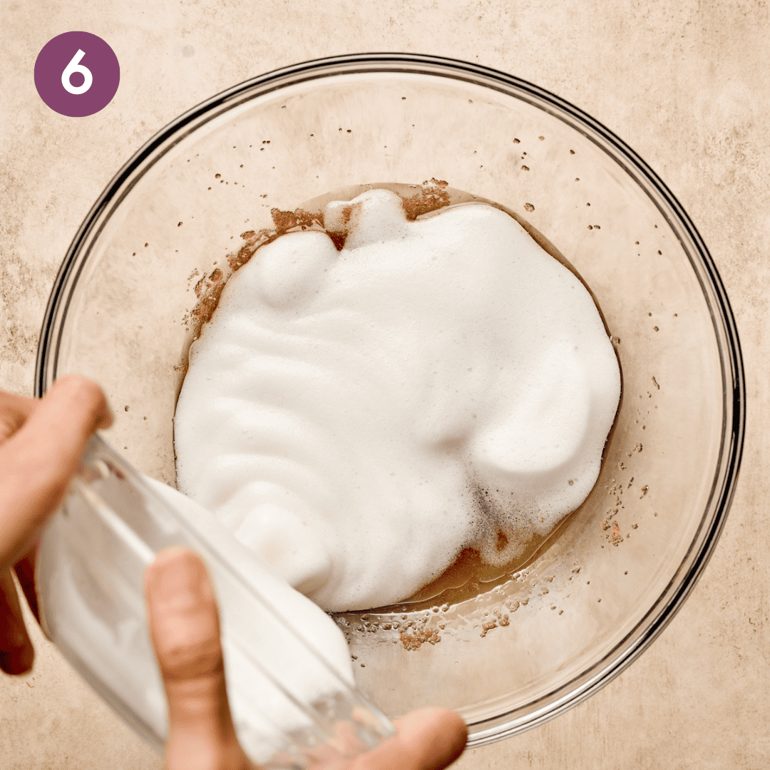 Person pouring whipped aquafaba onto brown sugar mixture in large bowl.