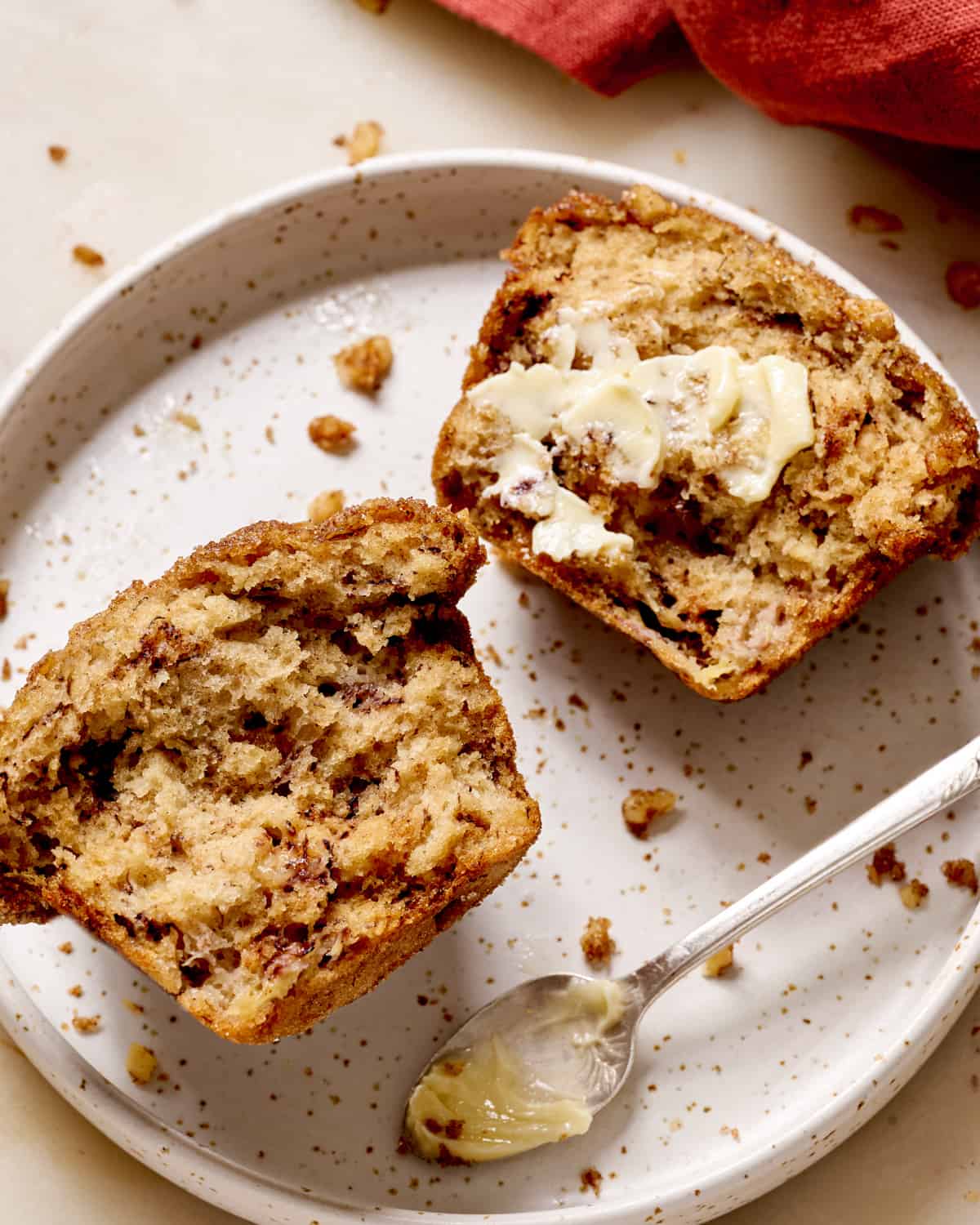 banana muffin sliced open and slathered with butter on a ceramic plate.