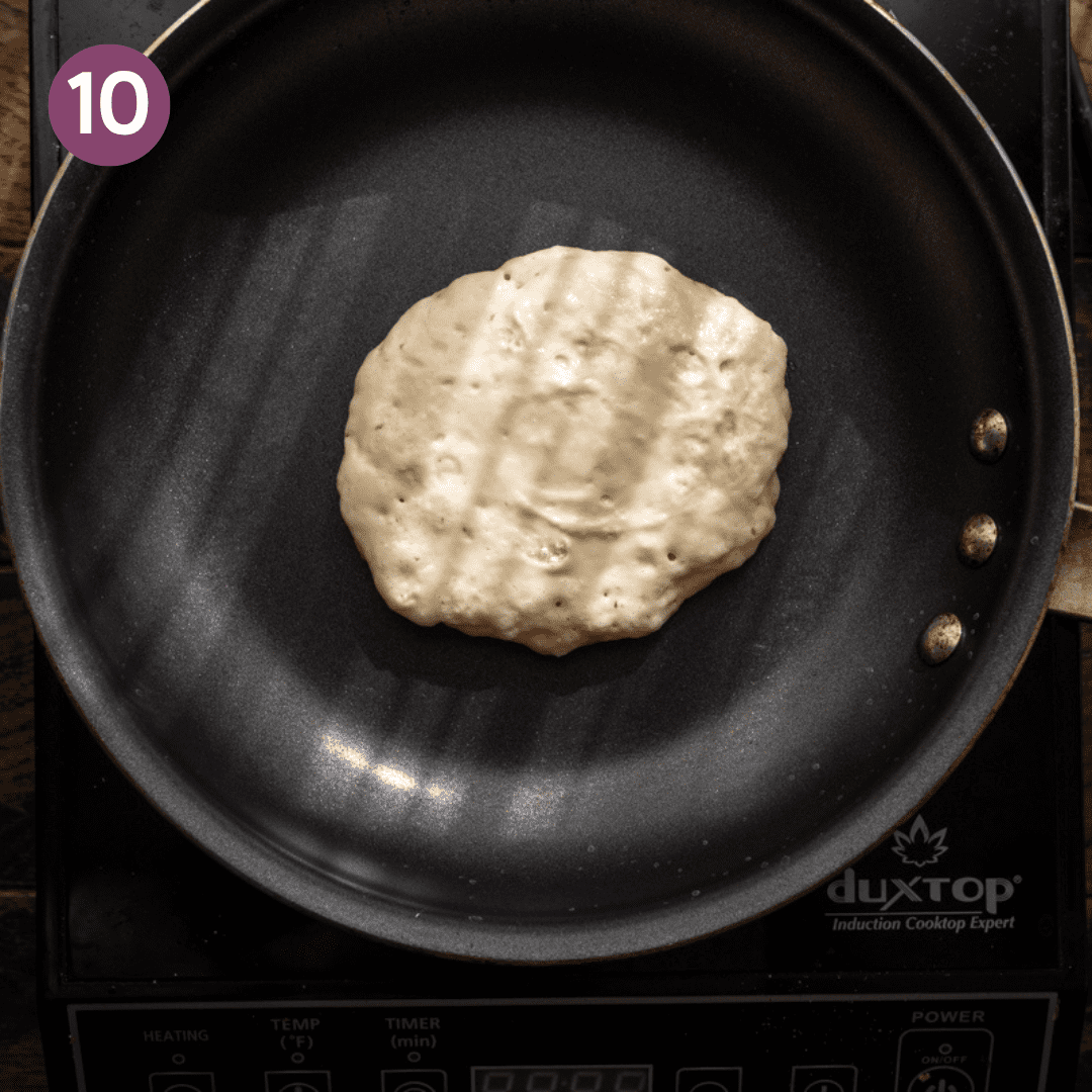 bubbles forming on a vegan pancake in a black skillet.