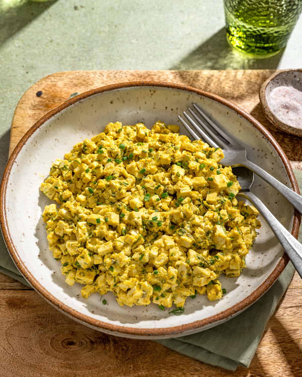 Vegan egg salad in a large white bowl on a wooden cutting board.