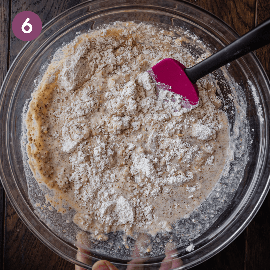 mixing dry and wet ingredients for muffin batter in glass bowl with silicone spatula.