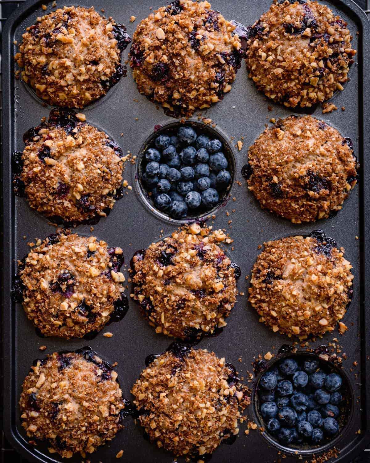 vegan blueberry muffins in muffin tin, with two muffins removed and filled with blueberries.