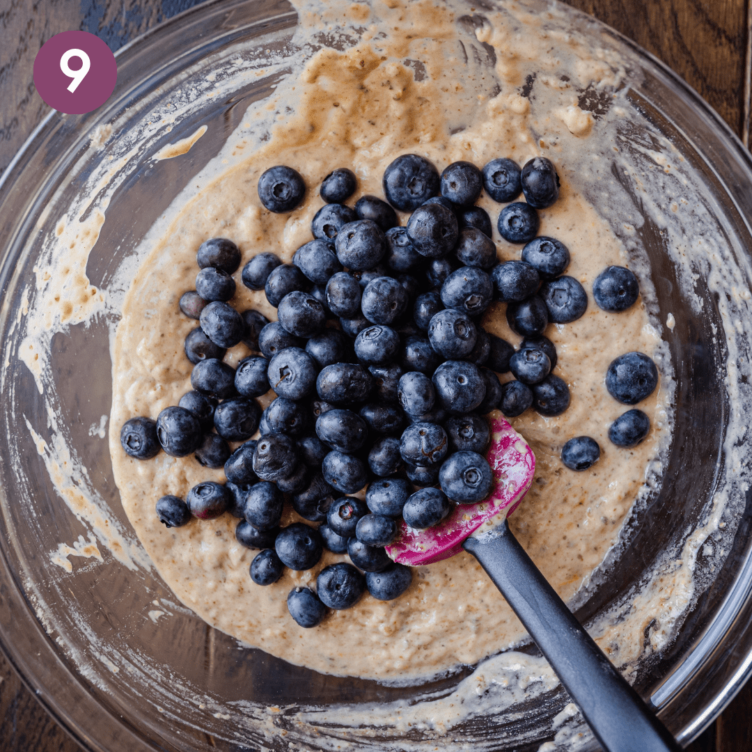 pile of blueberries sitting on top of muffin batter in glass bowl.
