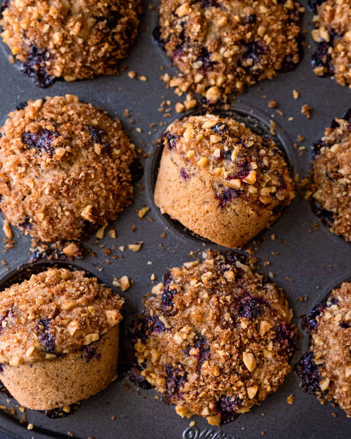 closeup of vegan blueberry muffins with walnut brown sugar crumble in muffin tin.