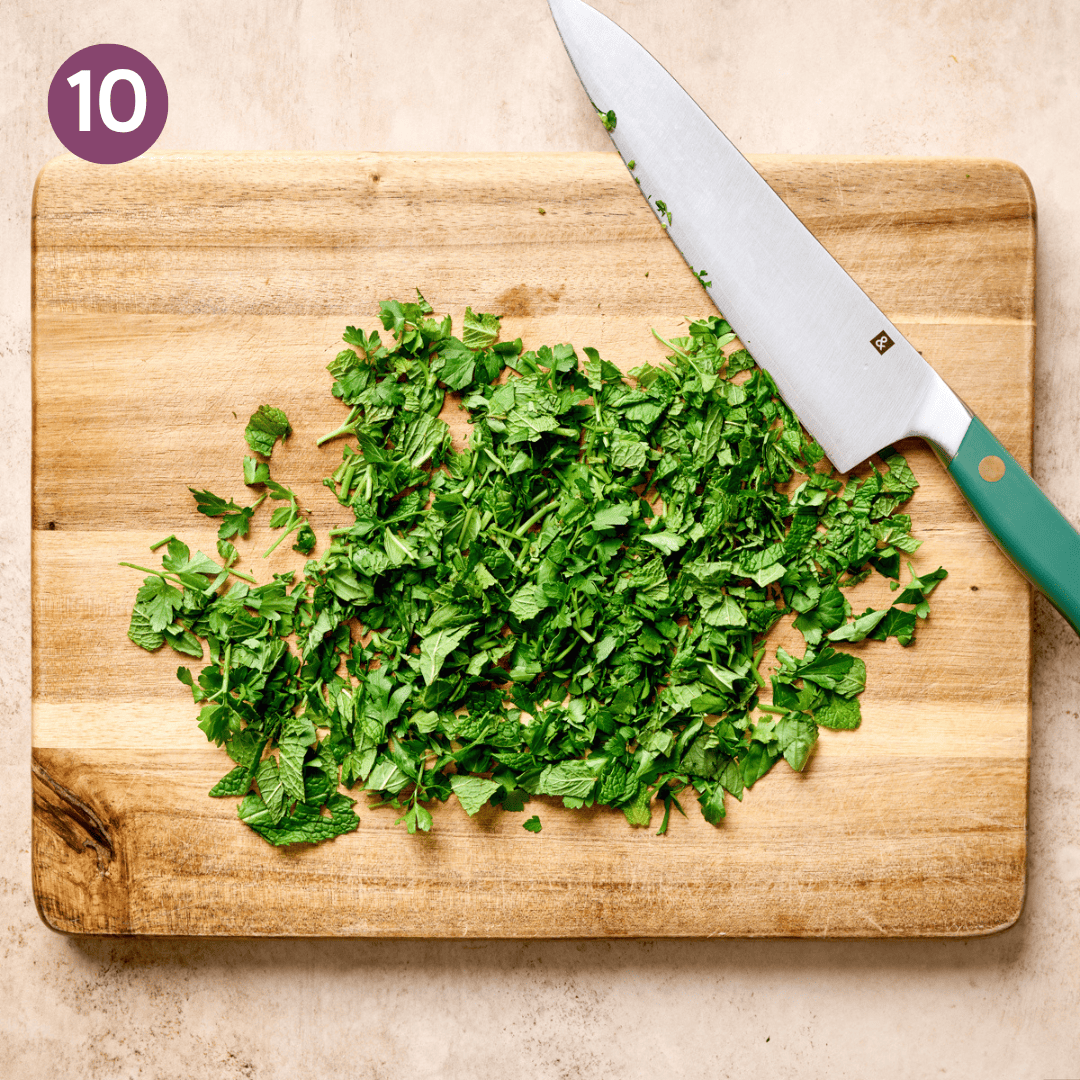 Chopped herbs and a knife of wooden cutting board.