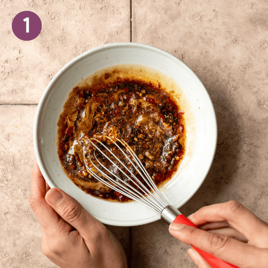 person using whisk to stir sesame sauce in a bowl.