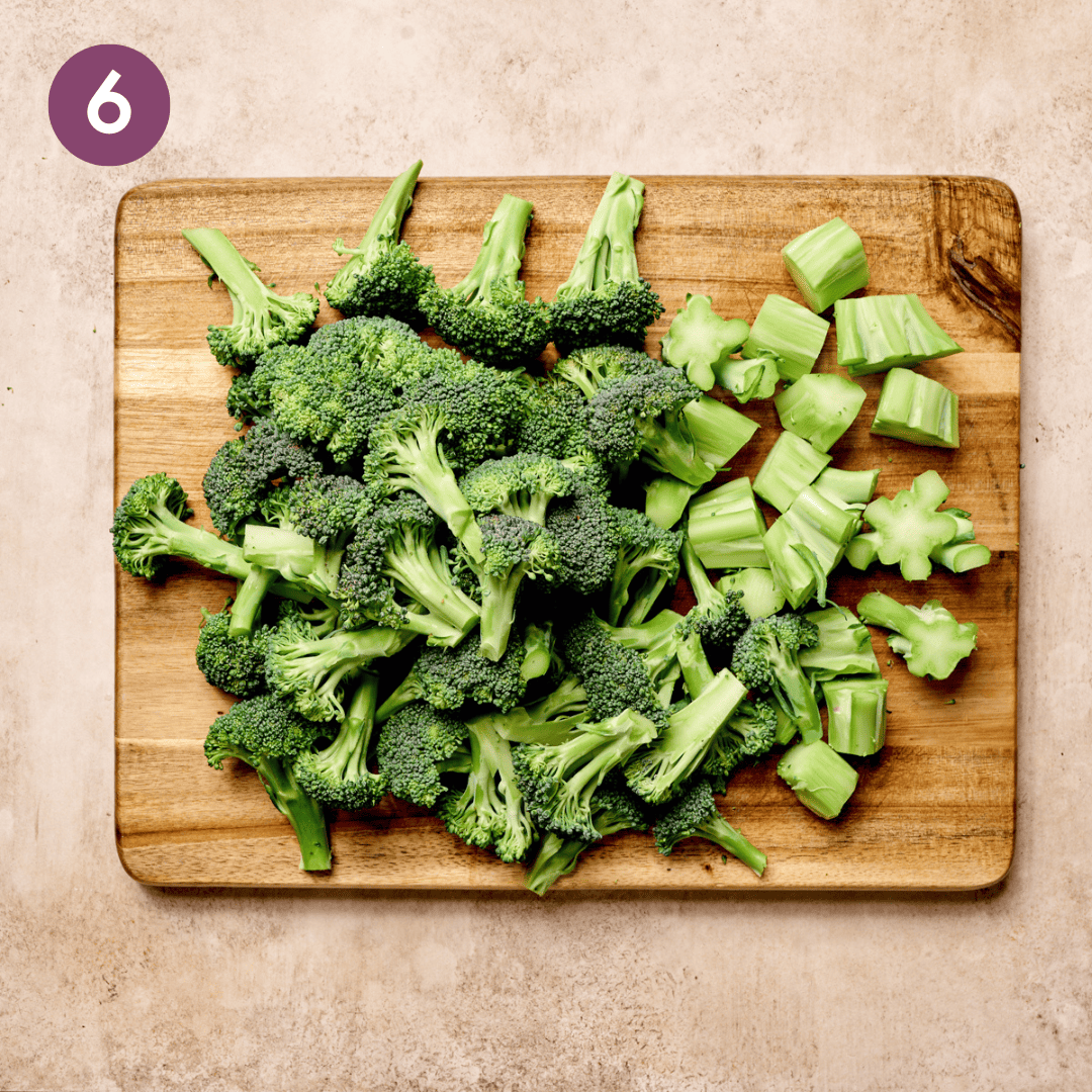 Roughly chopped stems and crowns of broccoli on a wooden cutting board.