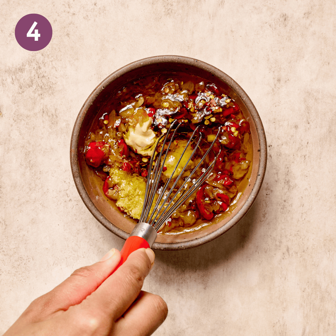 Person whisking pepper shallot mixture with other dressing ingredients in a bowl.