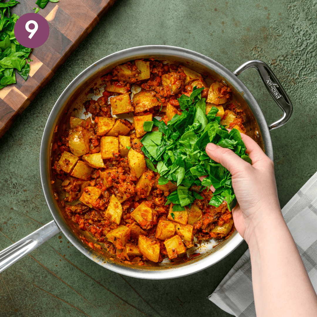 person adding baby spinach to the masala in the pan.