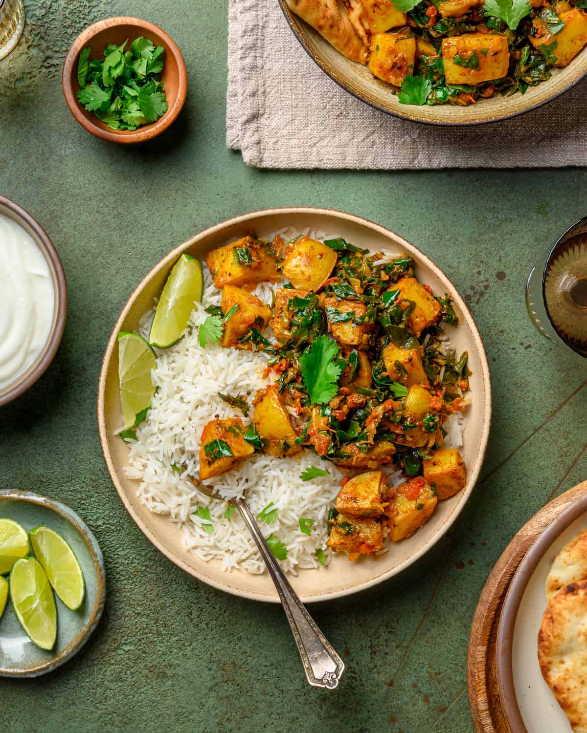 bowl of saag aloo with rice and lime wedges on a table.
