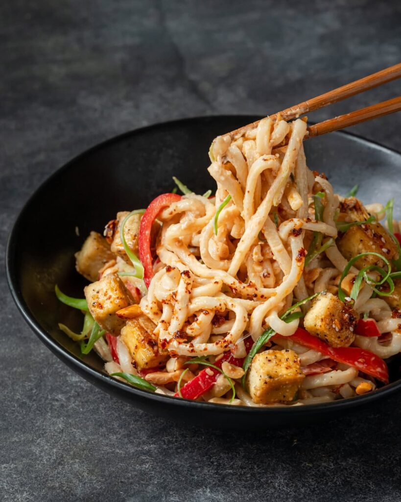 Peanut noodles with red peppers, green onions, tofu, and peanuts, drizzled with chili oil.