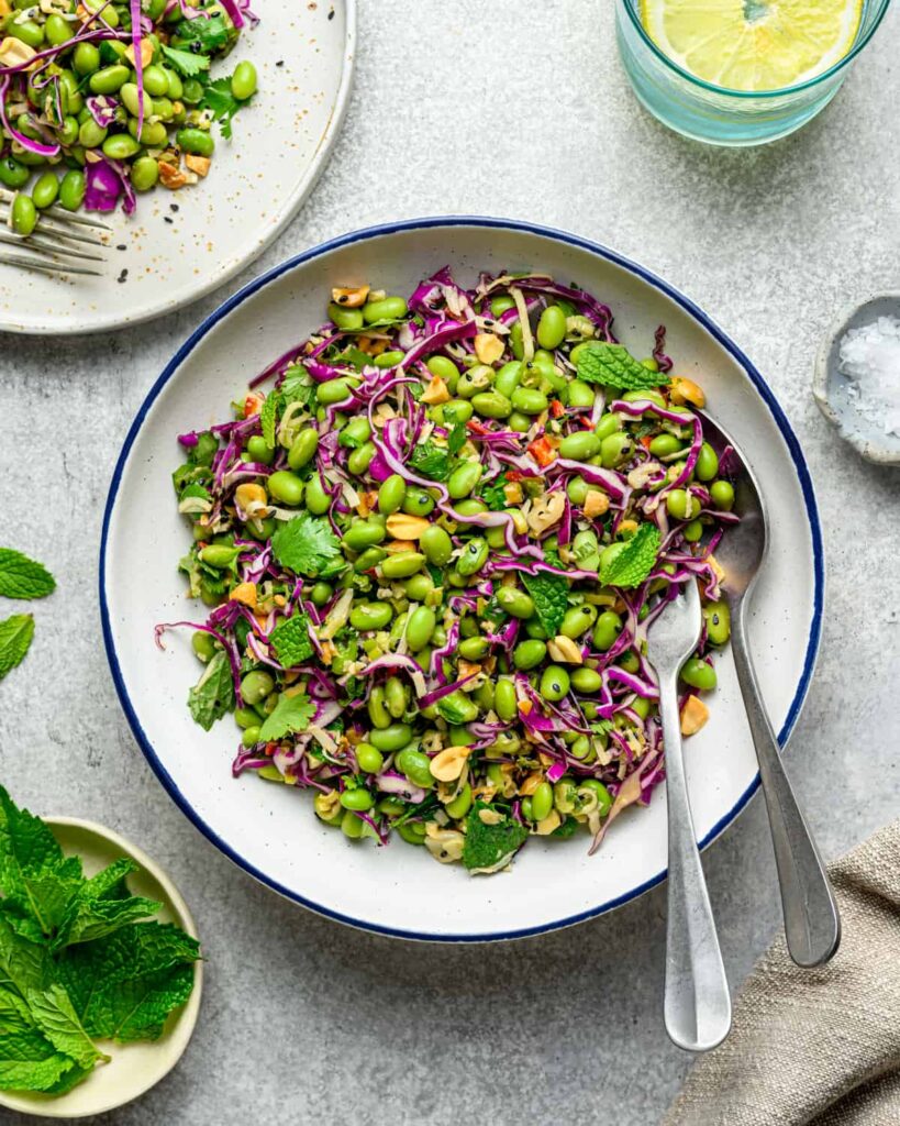 Bowl of edamame salad with two spoons on a white table.