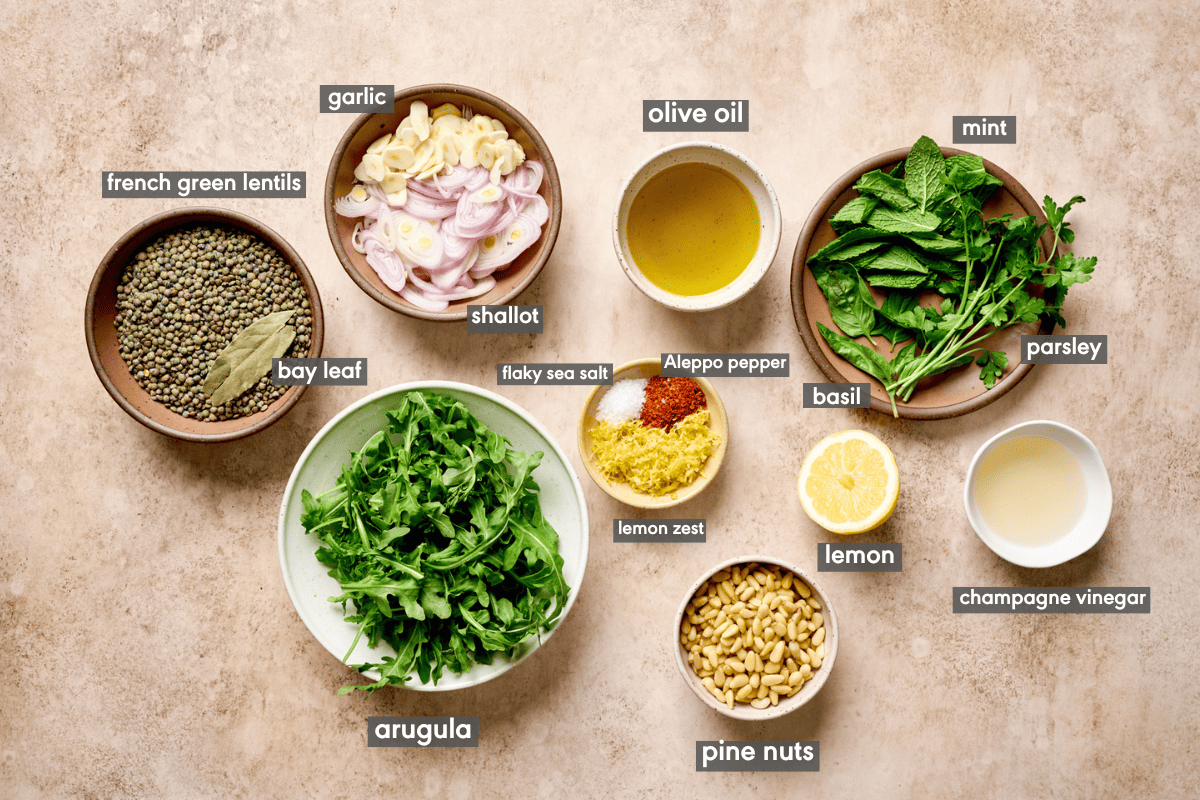 Lentil salad ingredients in various small bowls on a tan table.
