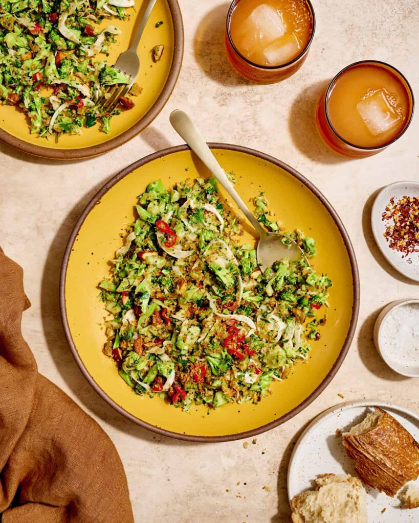 Close up side view of plate of broccoli salad on a yellow plate on a cream table.
