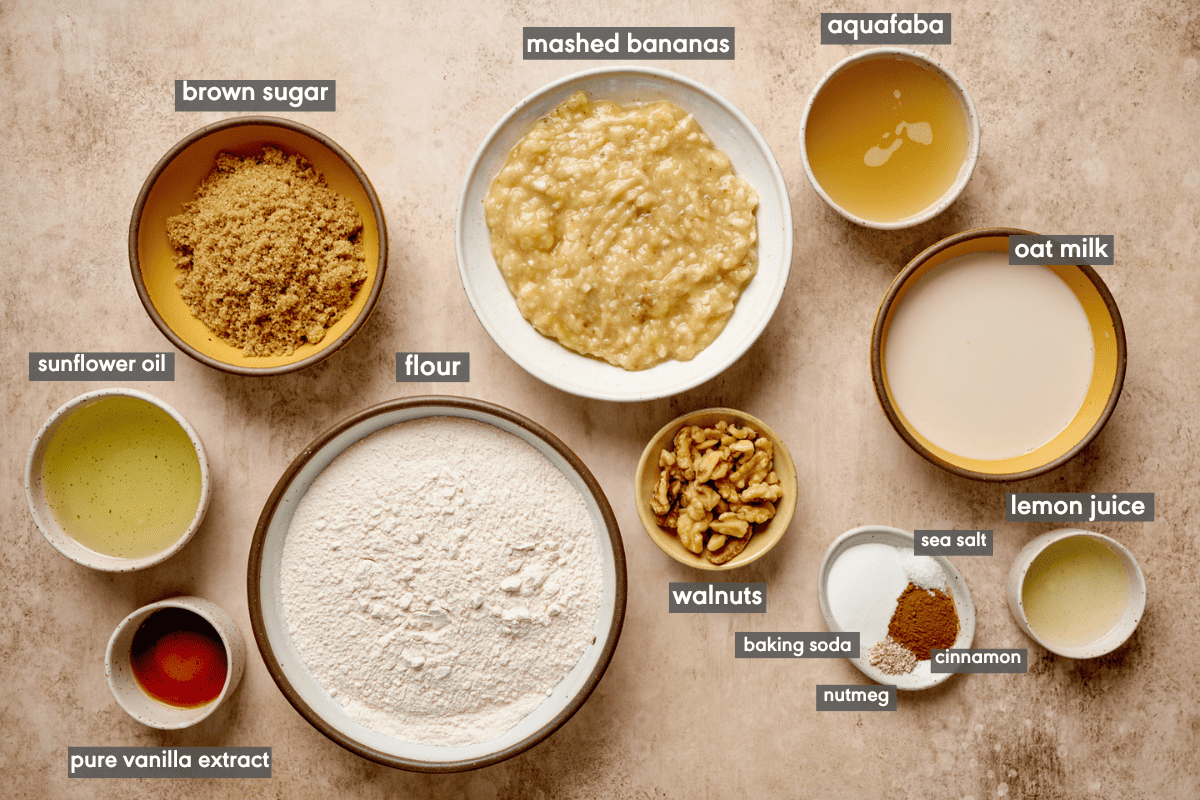 Various banana bread ingredients in small ingredient bowls on a tan table.